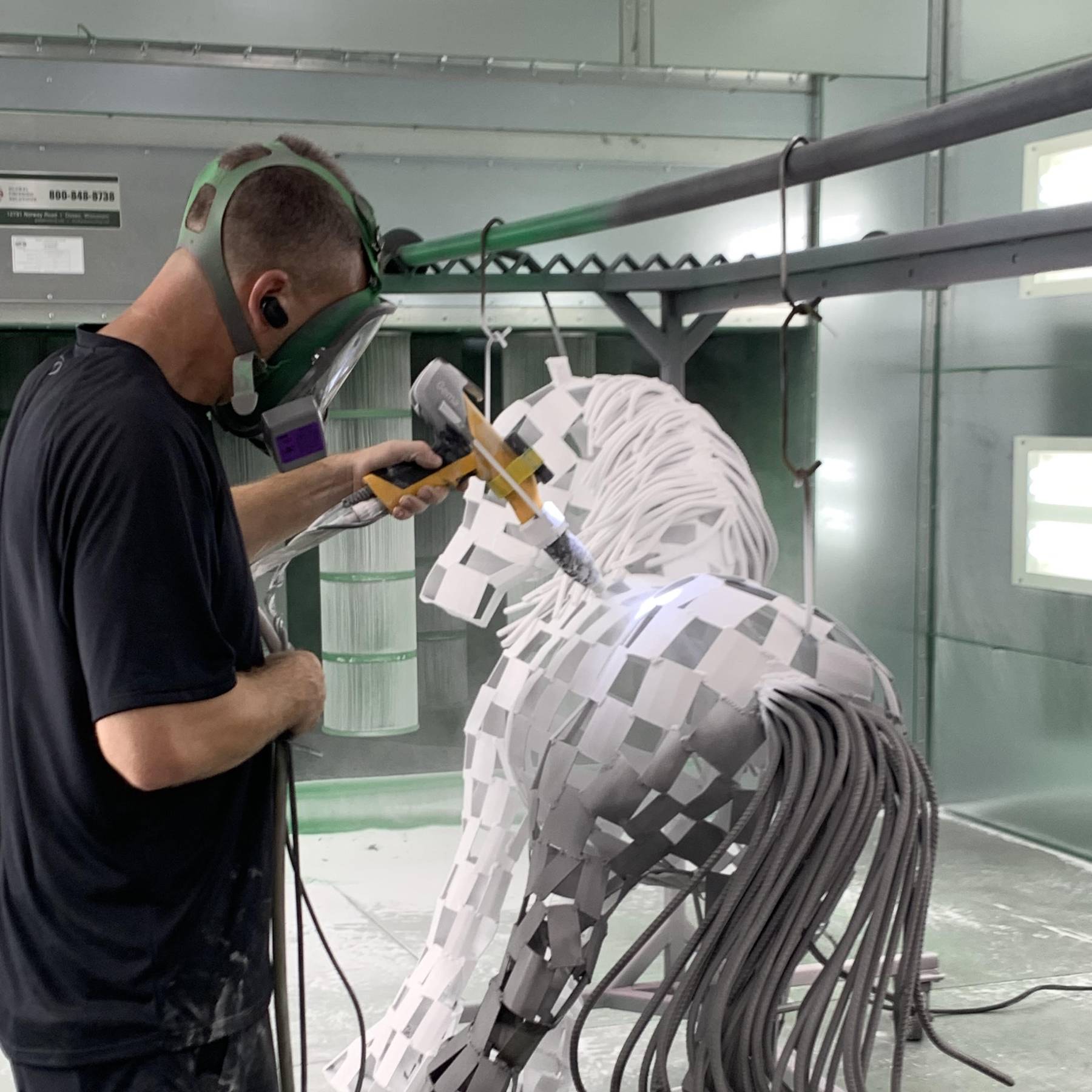 A man performs powder coating on a masked piece of work.