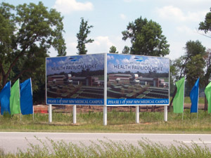 Side-by-sde-side signs of a map sitting a field with blue and green banners.