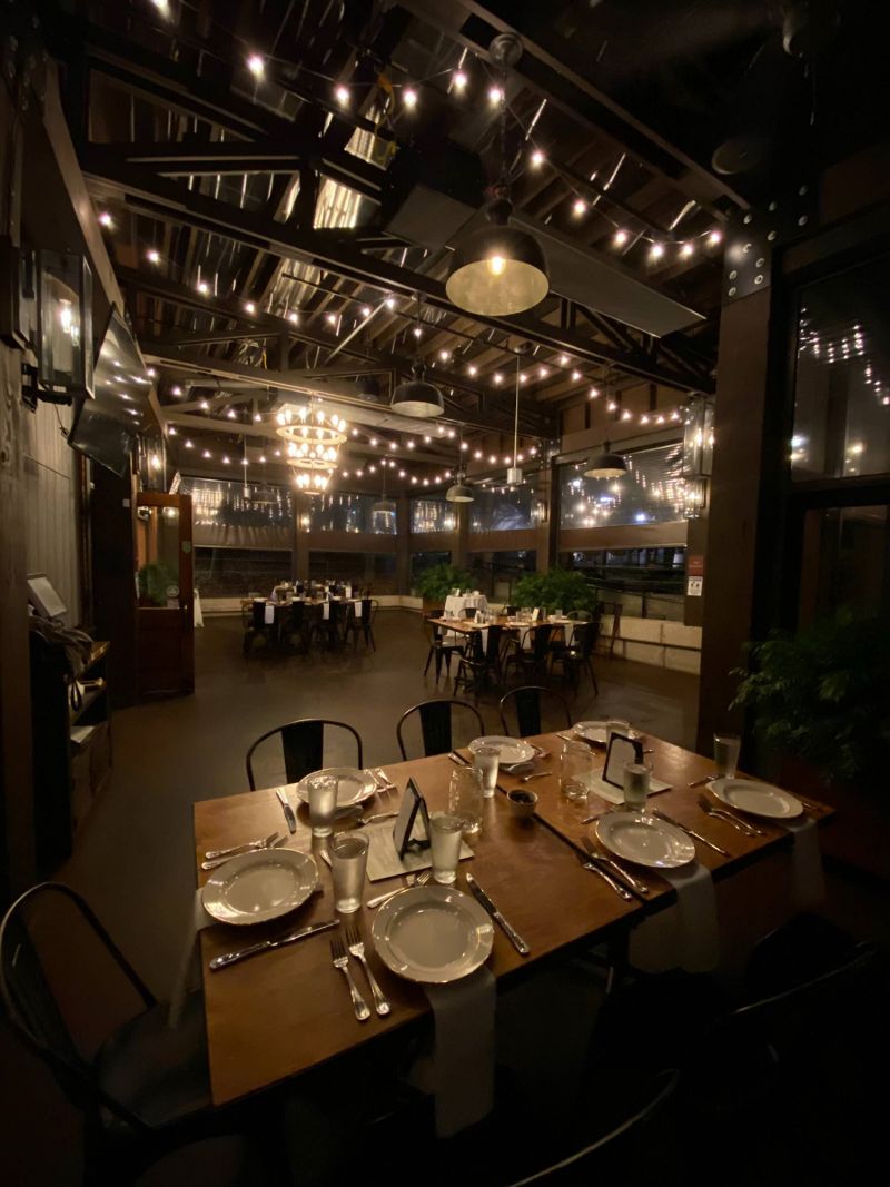 Patio space set up for a formal dinner at night, tables and chairs, cafe lights