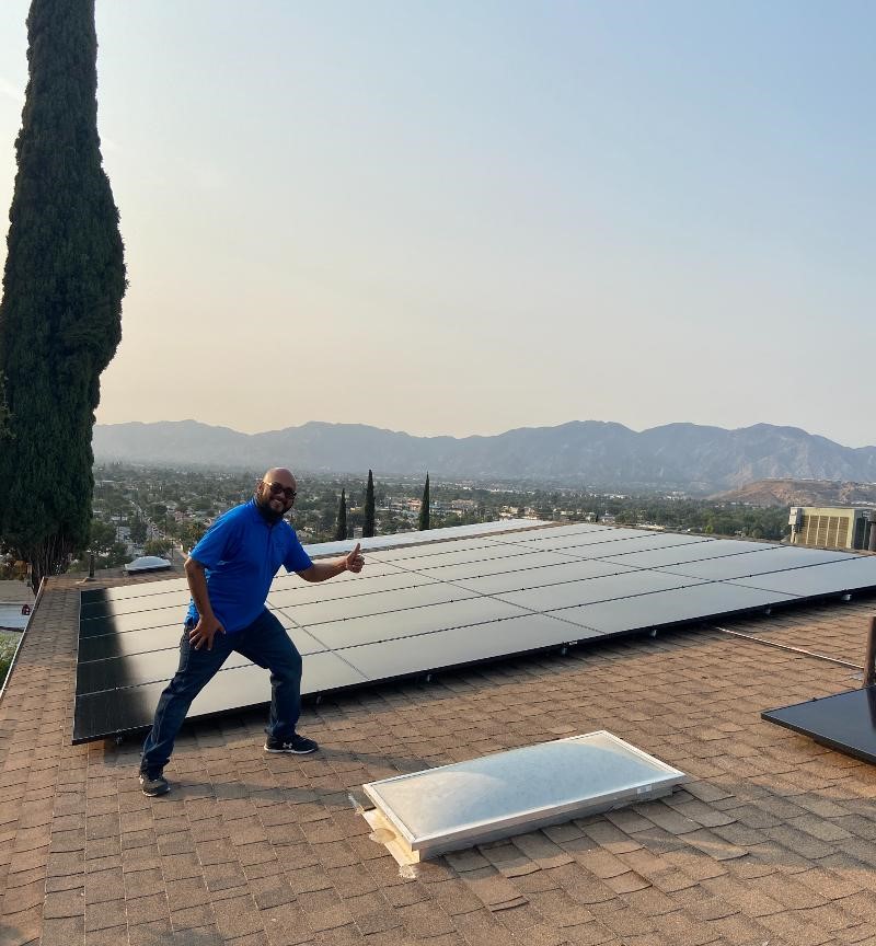 Owner of Tiger Stripe Solar smiling on a roof next to a residential solar panel system.