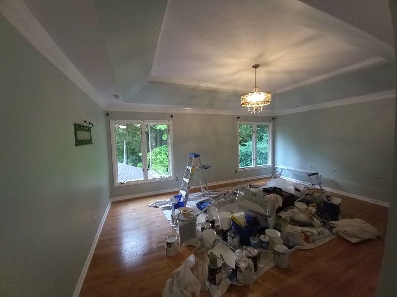 An empty living room freshly painted with paint supplies in the middle of the room.