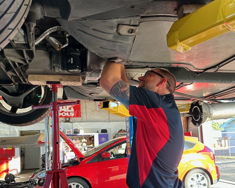 A mechanic works on the underside of a car on a lift.