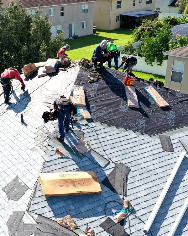 Construction workers install shingles on a gabled roof.