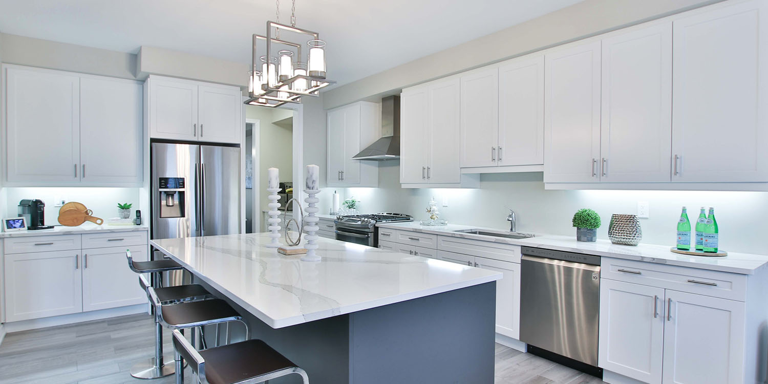 A modern kitchen with white cabinets and gray island with white countertop.