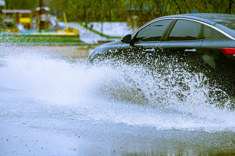 A car drives through standing high water in the roadway.