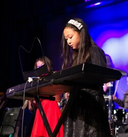 A young girl plays a keyboard on stage.