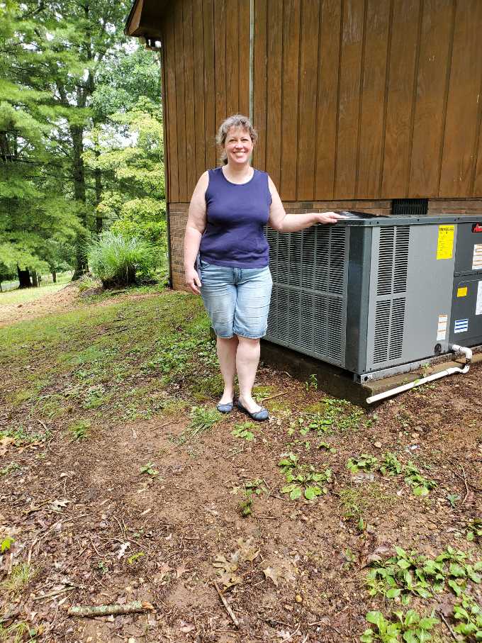 A woman stands next to an outdoor HVAC unit.