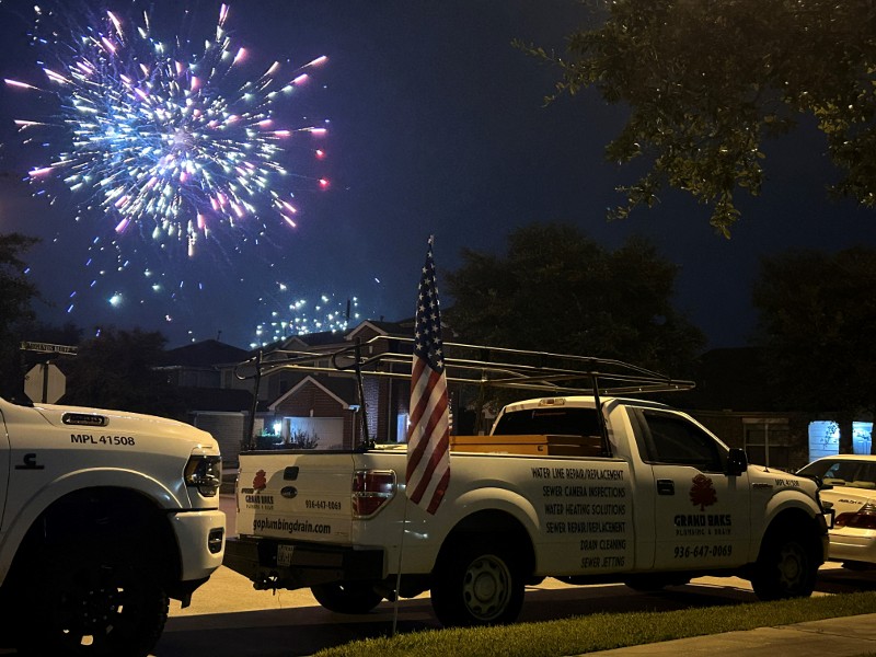 A Grand Oaks Plumbing pickup truck is parked while fireworks explode overhead.