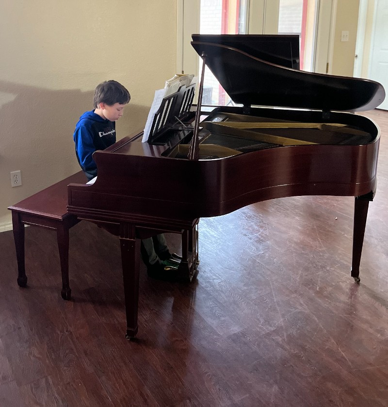 Young boy playing a grand piano.
