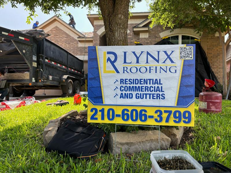 An advertising sign for Lynx Roofing leans against a tree.