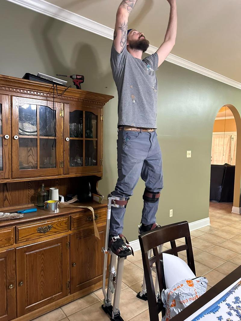A man on stilts performs work on a ceiling.