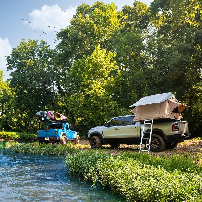 A truck with a camper top sits next to a creek.