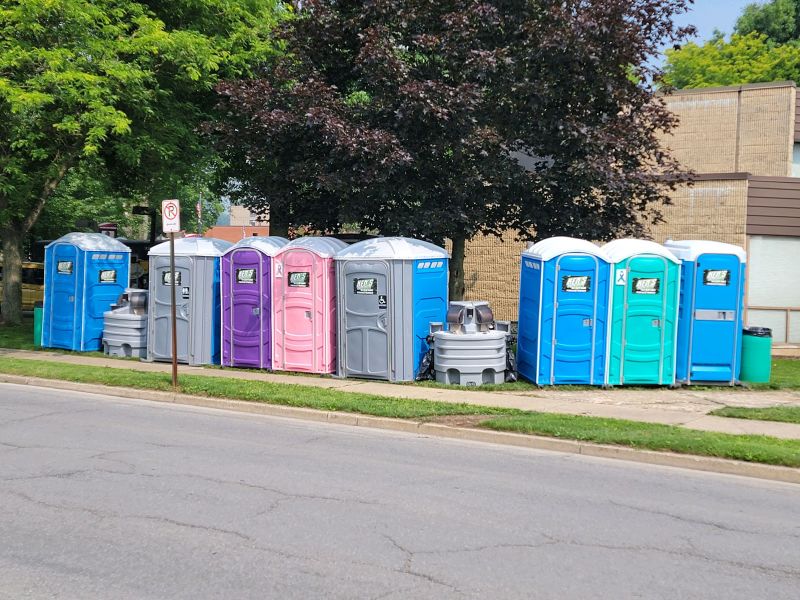 Eight portable toilets with two portable sinks situated in between them next to a roadway.