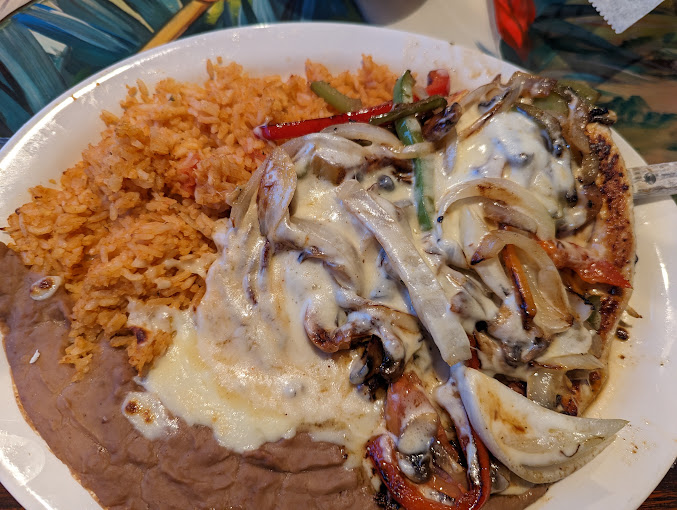 A plate of grilled vegetables covered in a queso sauce with refried beans and fried rice.