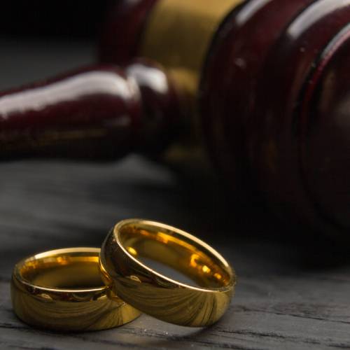 A close-up of two wedding rings with a judge's gavel behind them