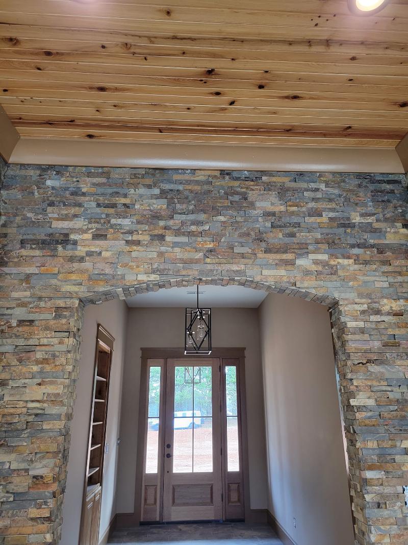 A home's entryway with a wood ceiling and stone tile wall.
