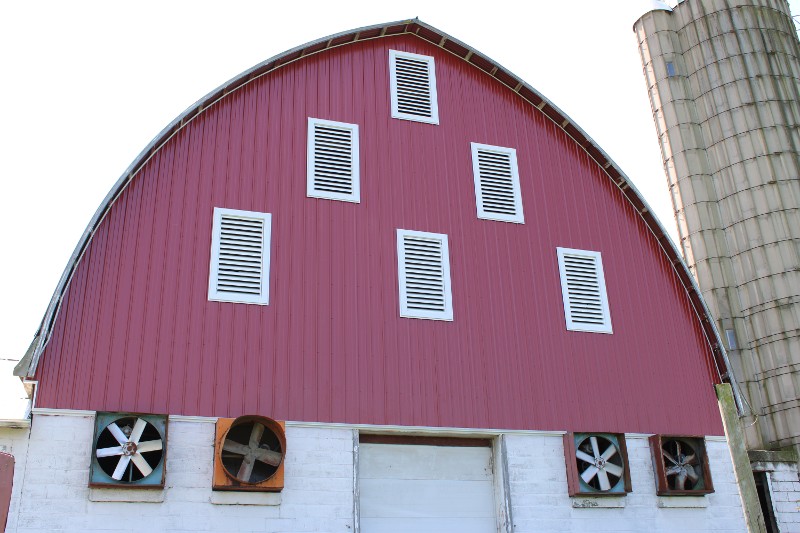 A red barn with rounded sides coming to a point and a silo to the right.