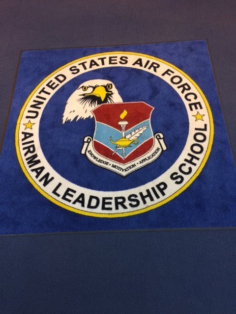 A blue rug with artwork for the U.S. Air Force Airman Leadership School.