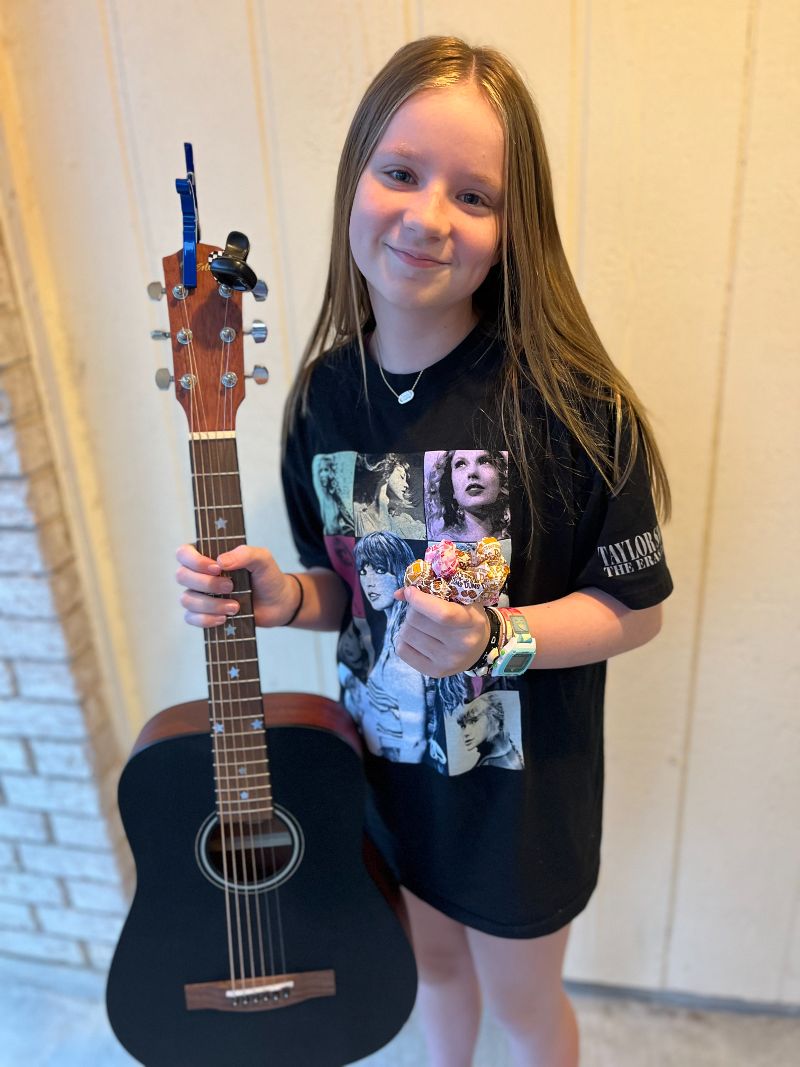 Young girl in a Taylor Swift t-shirt holding a guitar.