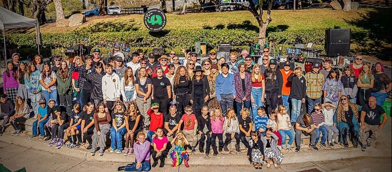 A large group of young musicians poses for a photo outside.