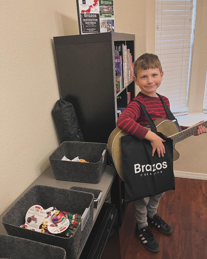 young boy poses with his guitar and a Brazos Creative tote bag.