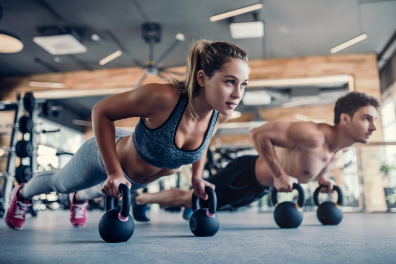 A man and woman do pushups over kettlebells.