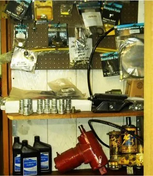 A shelf holding a drill, hydraulic jack, bottles of oil, and small accessories.