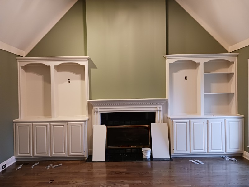 A freshly painted open space with white cabinets on either side of a fireplace.