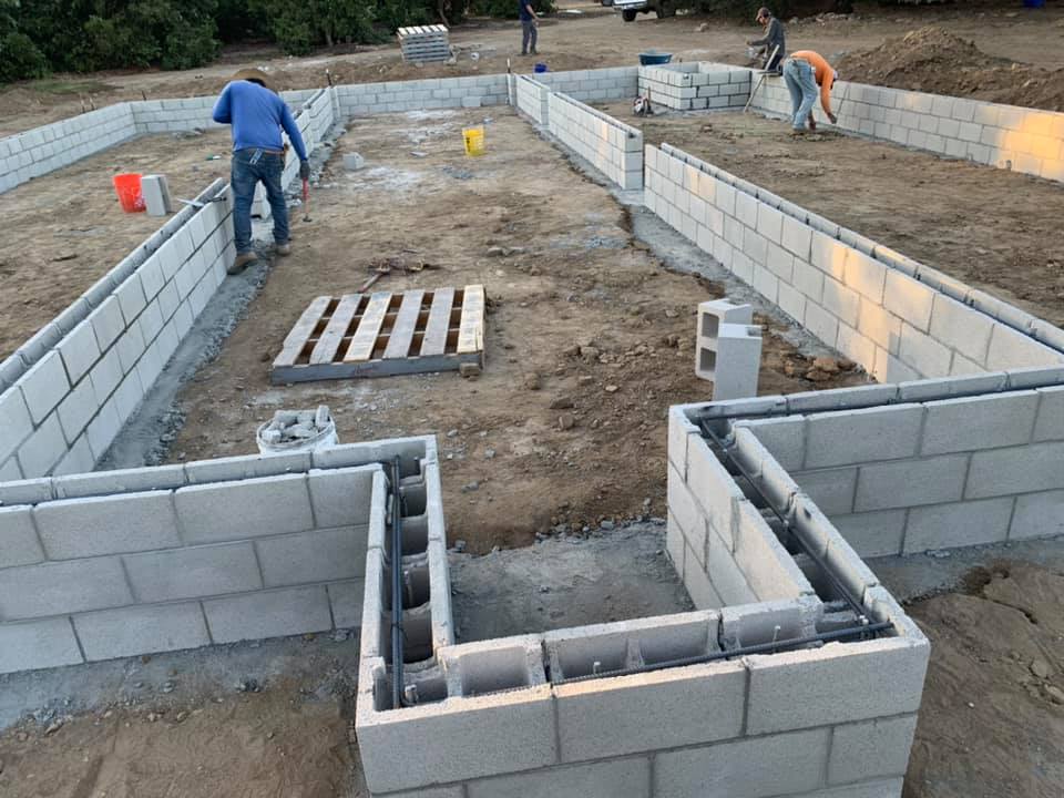 Two men work inside a home's foundation made of concrete blocks.
