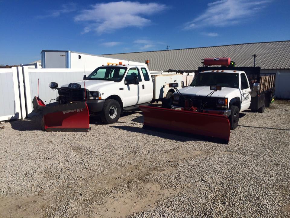 Two snowplow trucks sit in a gravel parking lot.