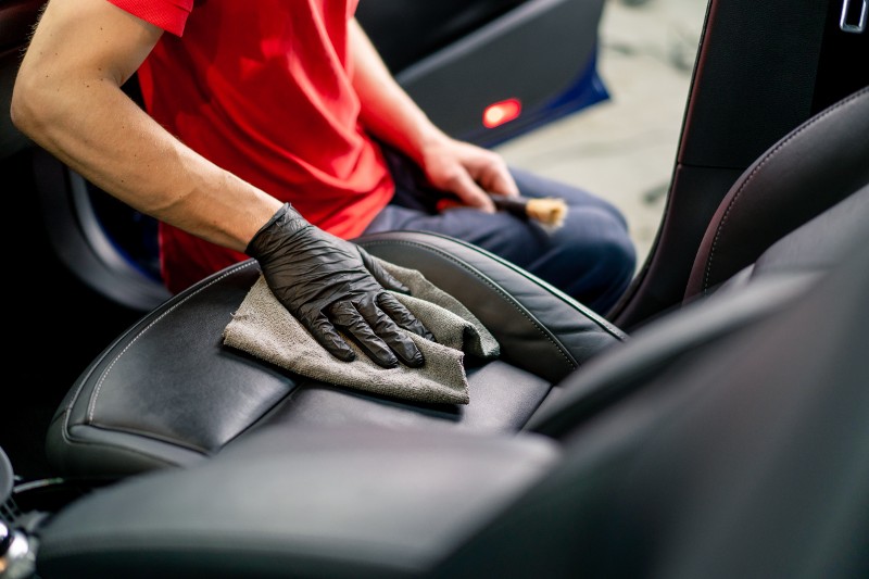 An auto detailer buffs leather seats inside a car.