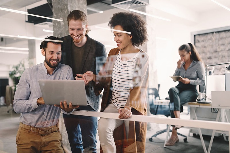 Business-Insurance-Portrait-of-a-Cheerful-Young-Group-of-Employees-Looking-at-a-Laptop-Together-While-Standing-in-a-Modern-Office-Space