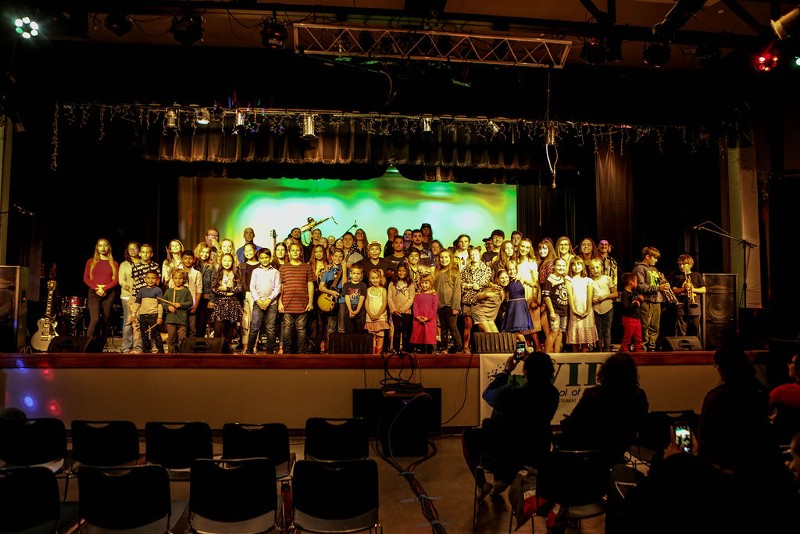 A large group of musicians poses on a stage.