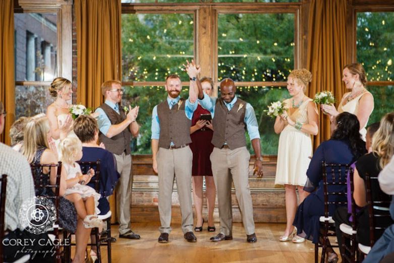 An interracial gay couple is married in an event venue, celebrated by friends and family