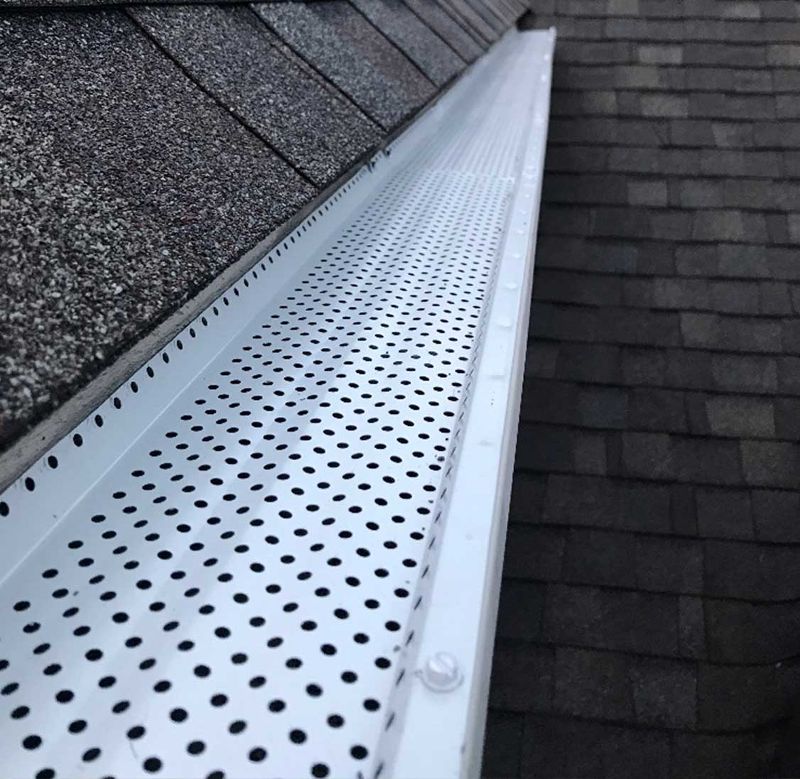 An open white gutter attached to a shigled roof.