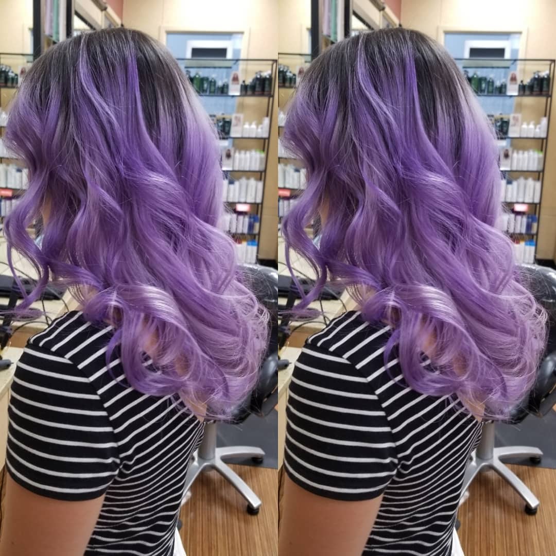 A woman with long, curly shows off her new purple hair color