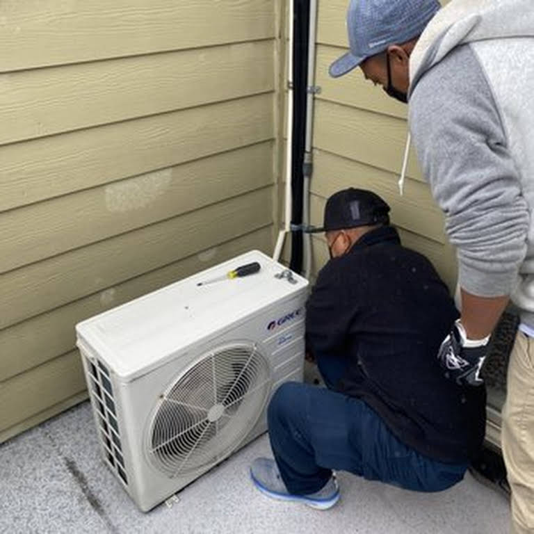 Two repair men inspect an exterior AC unit.