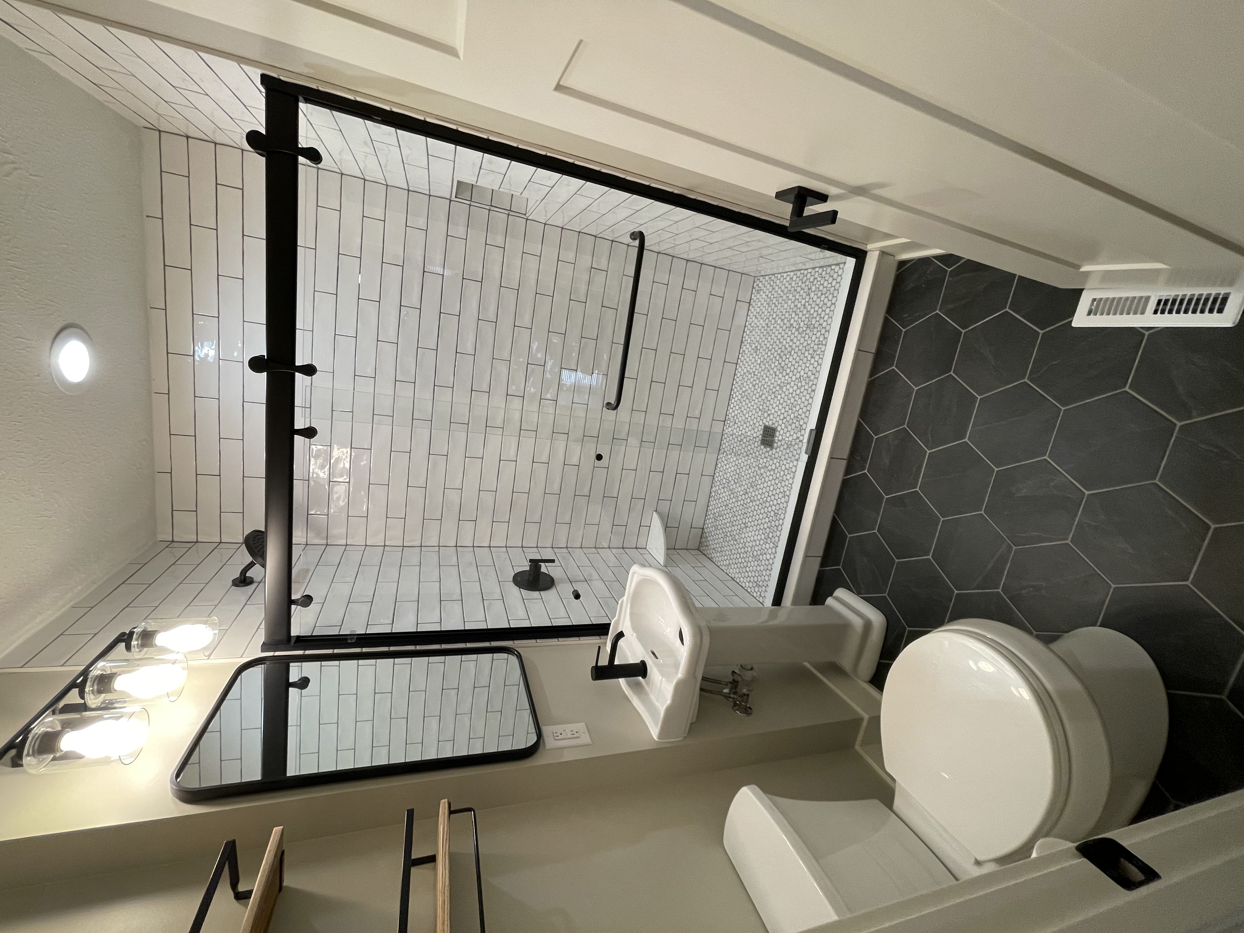 A modern bathroom with clear shower, white tile on of walls, and black tile on the floor