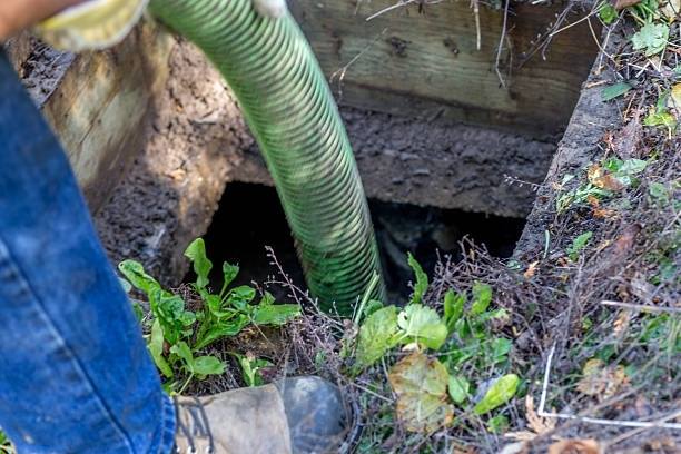 A septic pumper truck has a blue hose dropped into to the hole of a septic system at a commercial business.