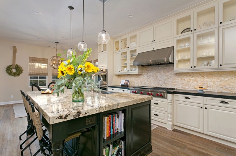 remodeled kitchen with wooden flooring, tile blacksplash, cream cabinets, dark creen lower cabinets and granite counter