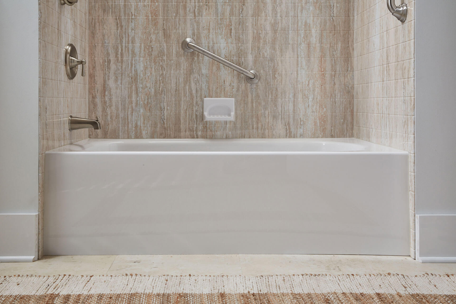 A soaker tub with a tile wall and a grab bar on the wall.