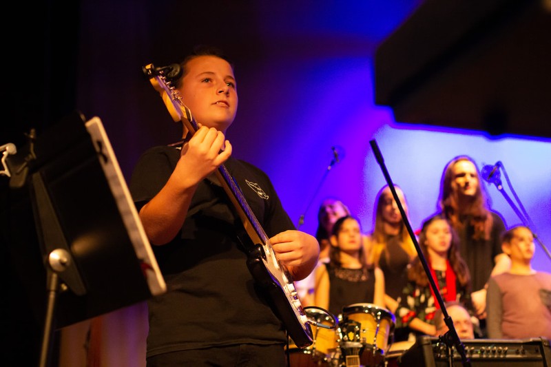 A boy plays a guitar on stage.