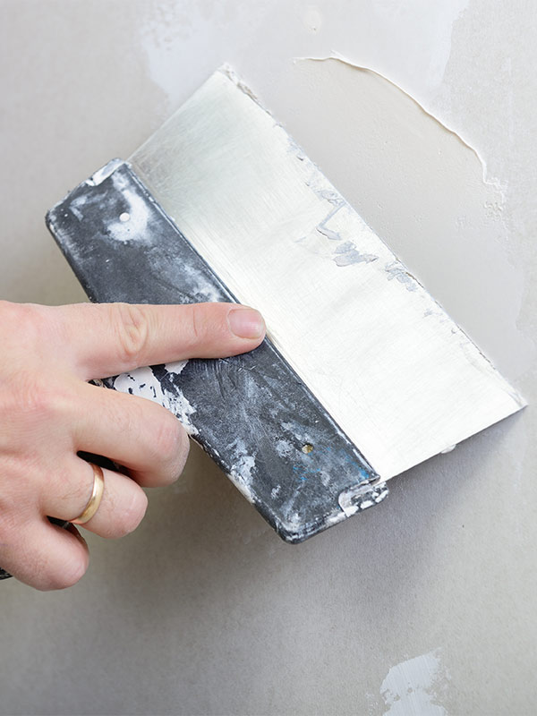 Hand applying spackle to drywall.