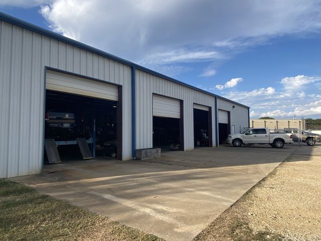 A white pickup truck sits outside a four-bay repair shop.