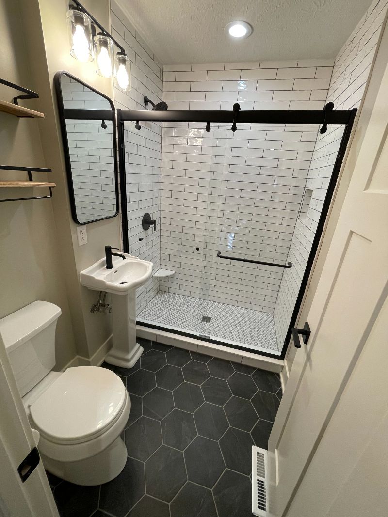 A modern bathroom with clear shower, white tile on of walls, and black tile on the floor