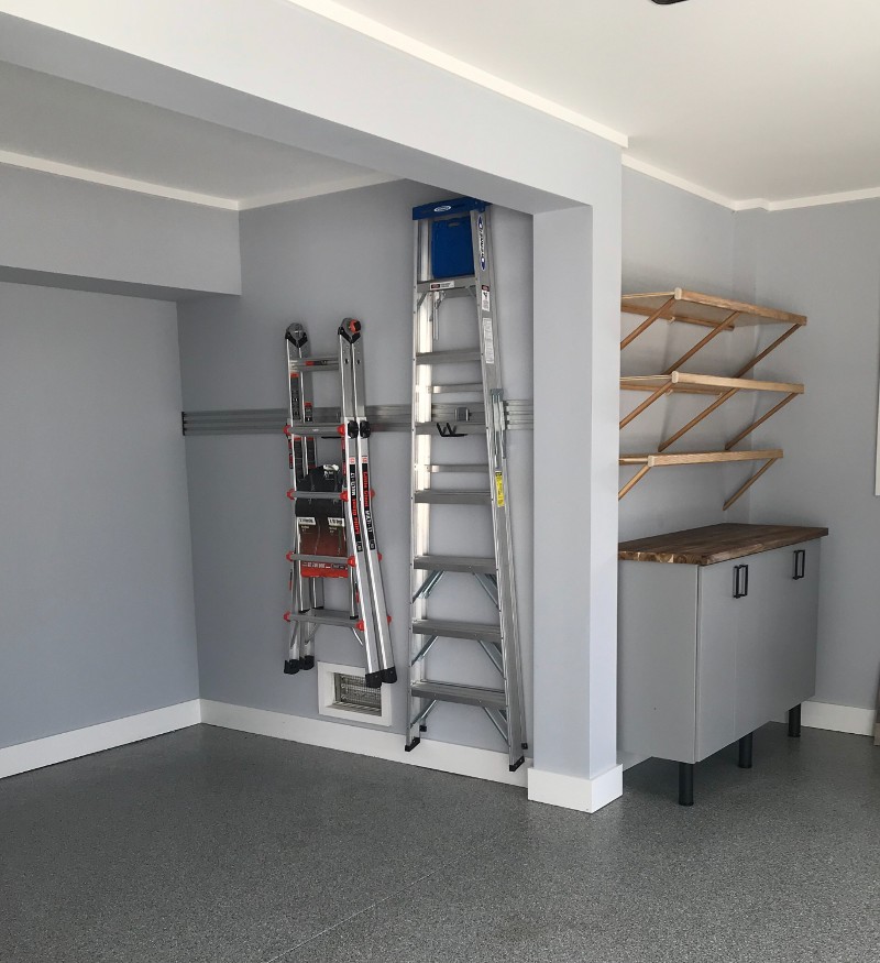 A storage section in the corner of a garage with ladders hanging on the wall.