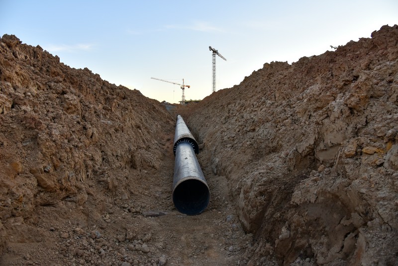 A utility pipe lays in a dug trench.