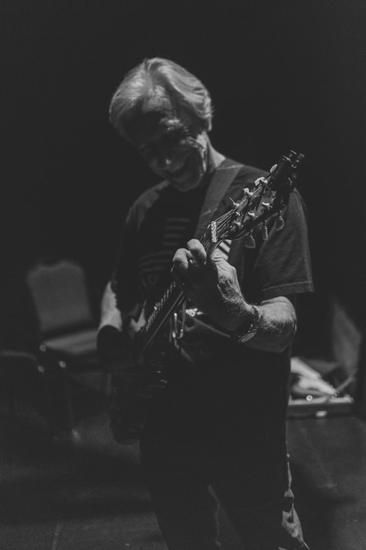 A man smiles while playing a guitar.