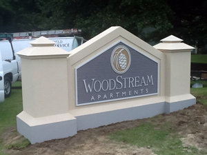 Outdoor signage between white columns for WoodStream Apartments.
