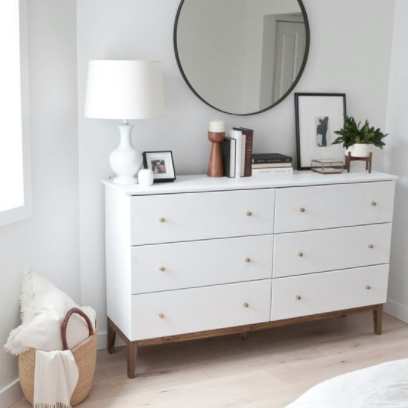 A white dresser with a round mirror above it. 